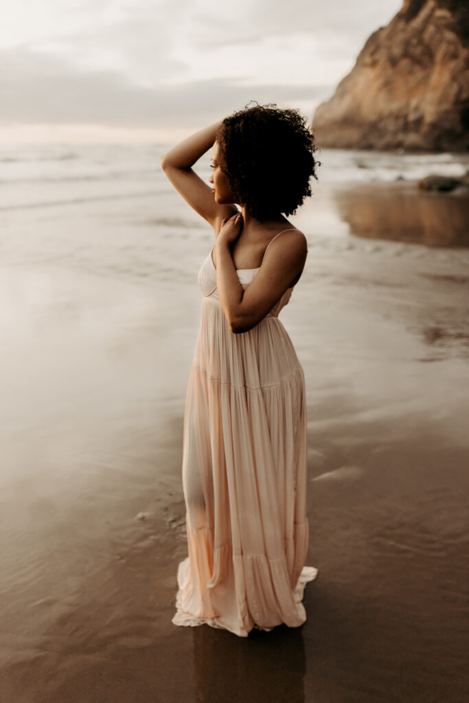 Family Photography, woman standing in the sand next to the ocean with her hand in her hair